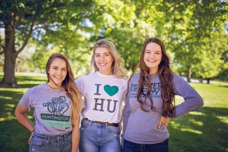 Three girls are standing in the grass at Huntington University wearing HU t-shirts.