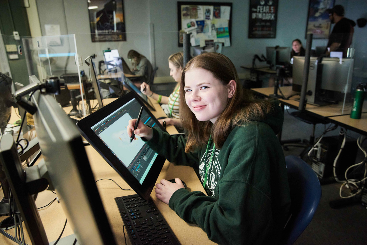 An animation student smiles next to a pen tablet.