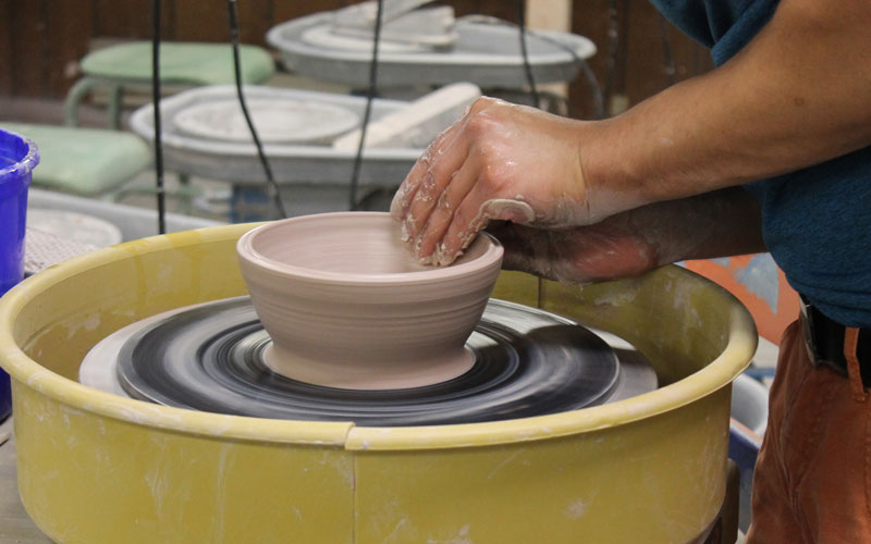 A detailed image of a pair of hands delicately sculpting clay on a potter's  wheel during a soft-lit evening in a pottery studio, captured with a medium  format camera using a macro