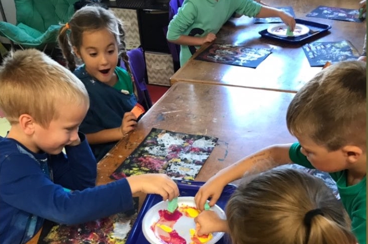 Four children working on an art project together in a classroom setting.
