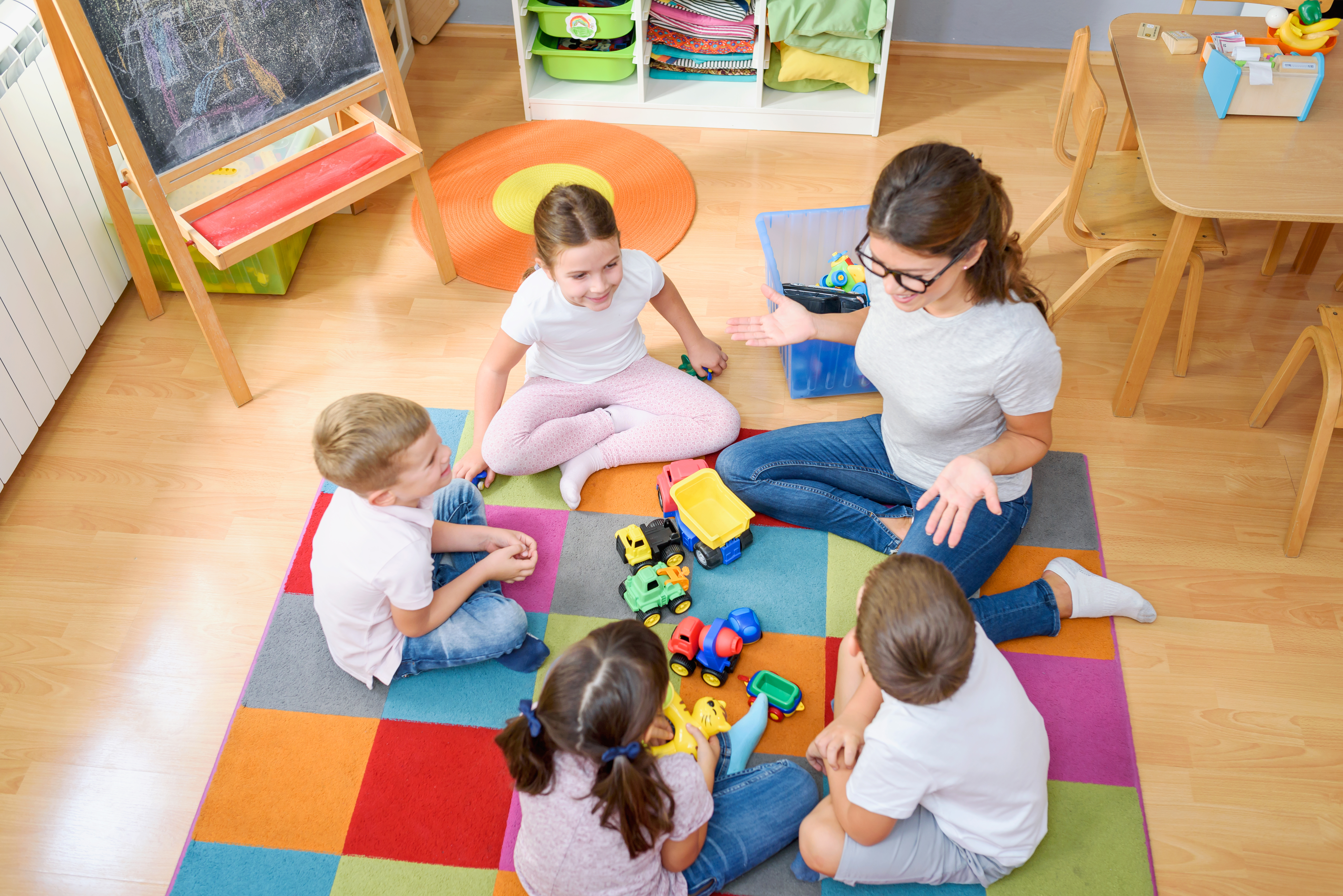 A top down view of a teacher on the floor with 4 of her young students.