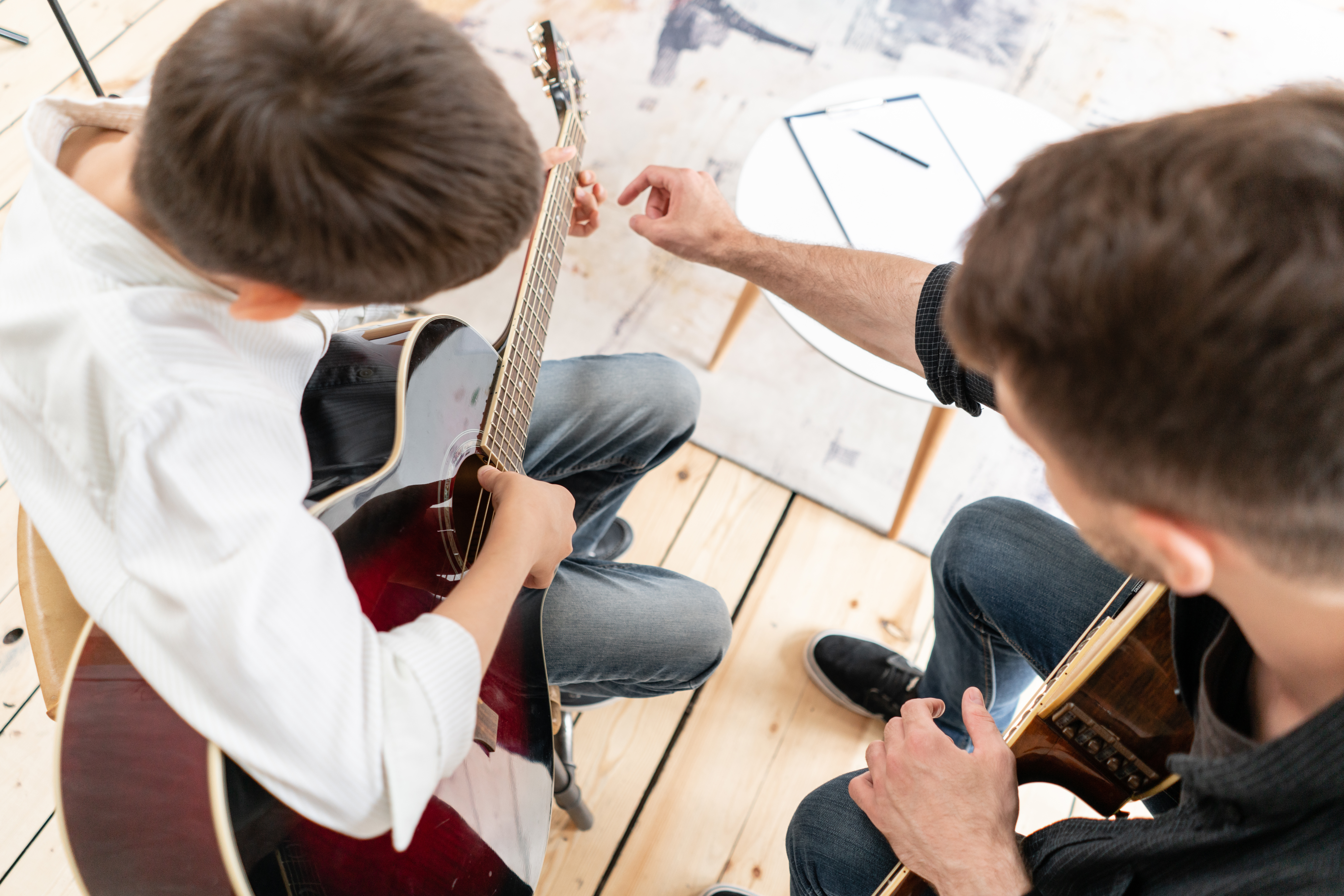 A top-down view of an instructor teaching a student acoustic guitar.