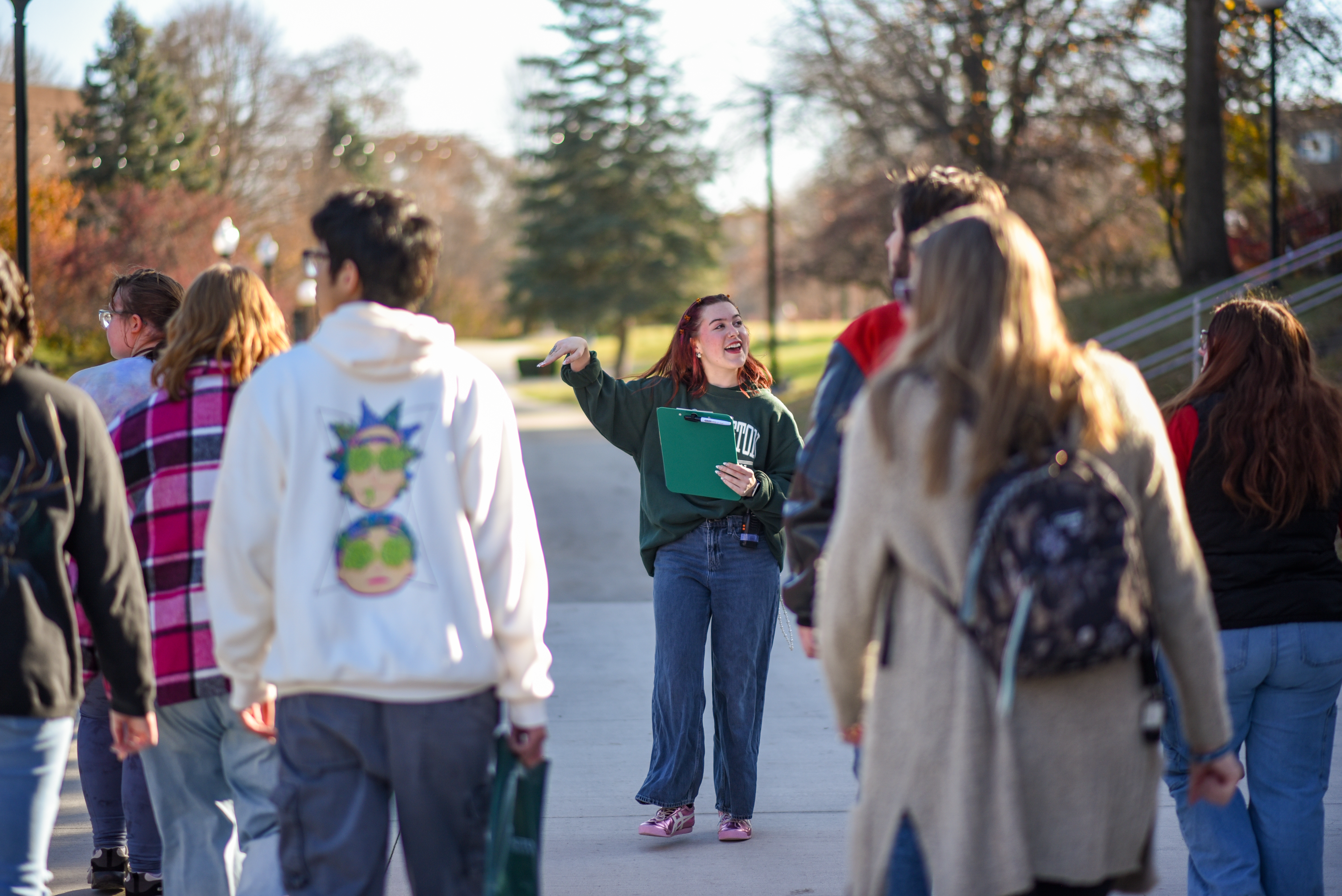 A group of students visit campus. The person in the center leading them is holding a clipboard.