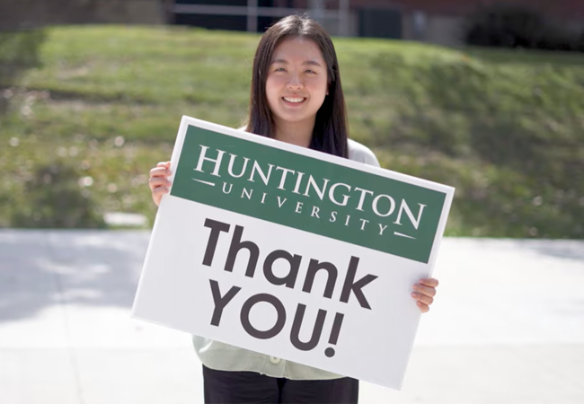 Picture of a girl holding a sign that says Thank You with a smiley face while standing in the hallway of the Merillat Centre for the Arts at Huntington University.