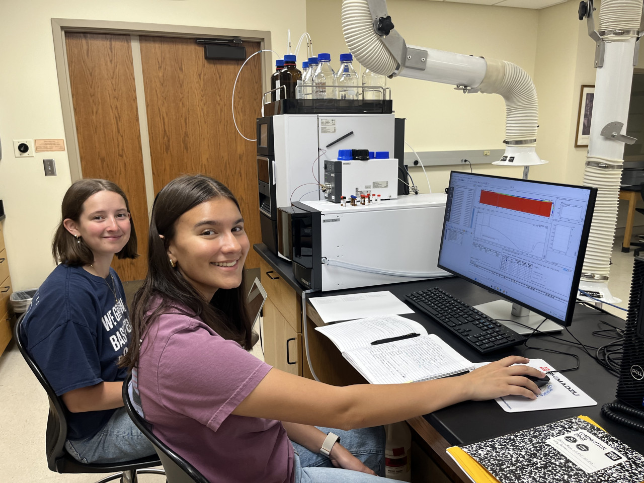 Two females smiling for the camera while working in a chemistry laboratory